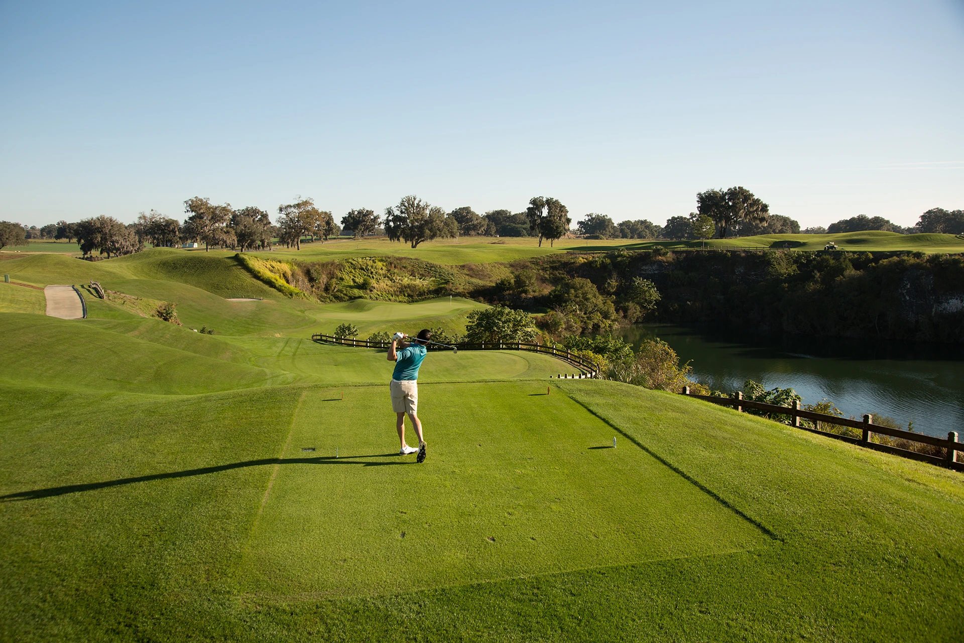 Golfer teeing off above rolling fairways, quarry terrain, and water at The Club at Iron Lake in Ocala, Florida.