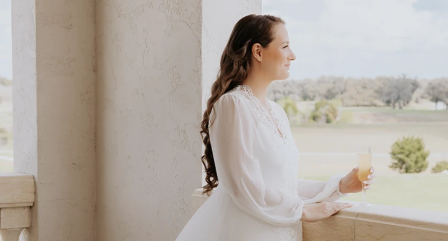 Bride in a white robe holds a drink on a clubhouse balcony overlooking the grounds in Ocala, Florida.