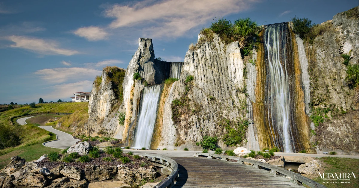 Dramatic limestone cliffs with cascading waterfalls frame a winding boardwalk path at Altamira residential development, showcasing its breathtaking natural